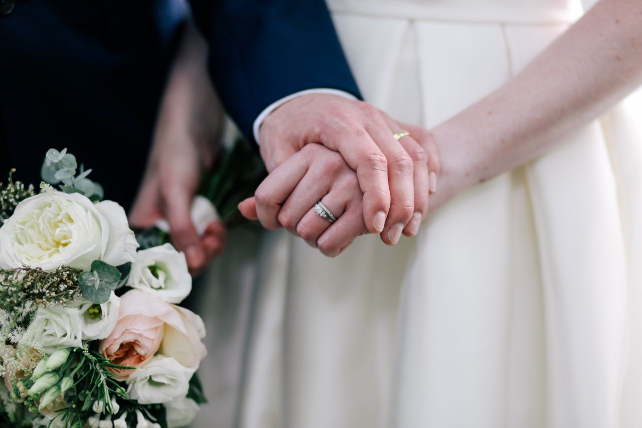 A bride and groom hold hands, showing their wedding rings.