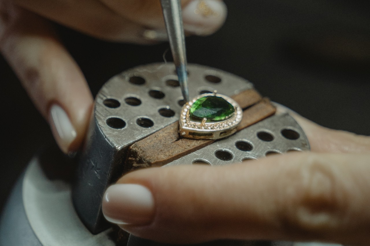 a jeweler sets an emerald in a prong setting for a pendant.