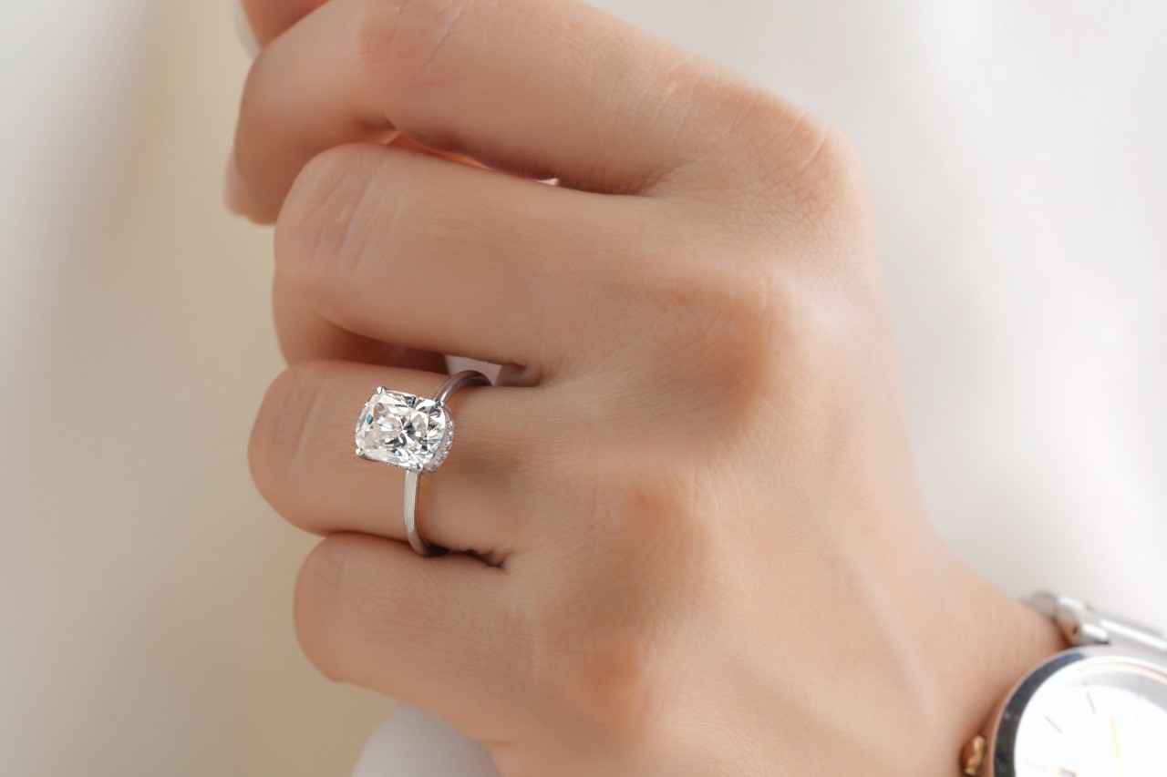 close up image of a woman’s hand wearing a silver solitaire diamond engagement ring