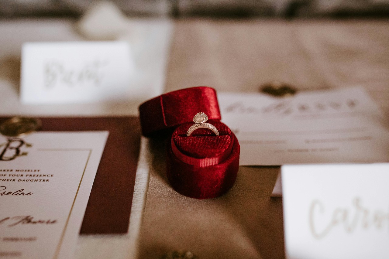 a red ring box on a careful set table featuring a yellow gold diamond engagement ring