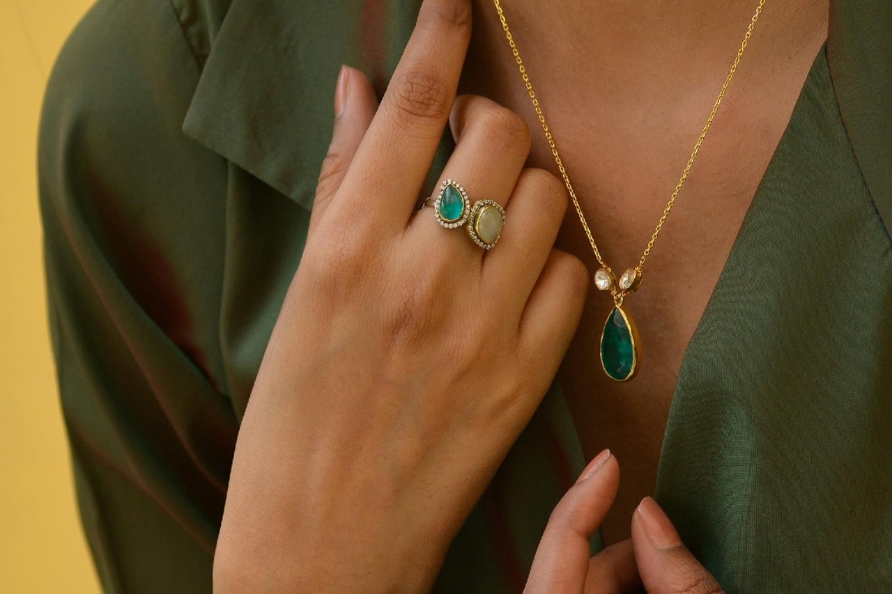 Close up of a person in a green blouse showcasing a teardrop green gemstone pendant and a two stone ring.