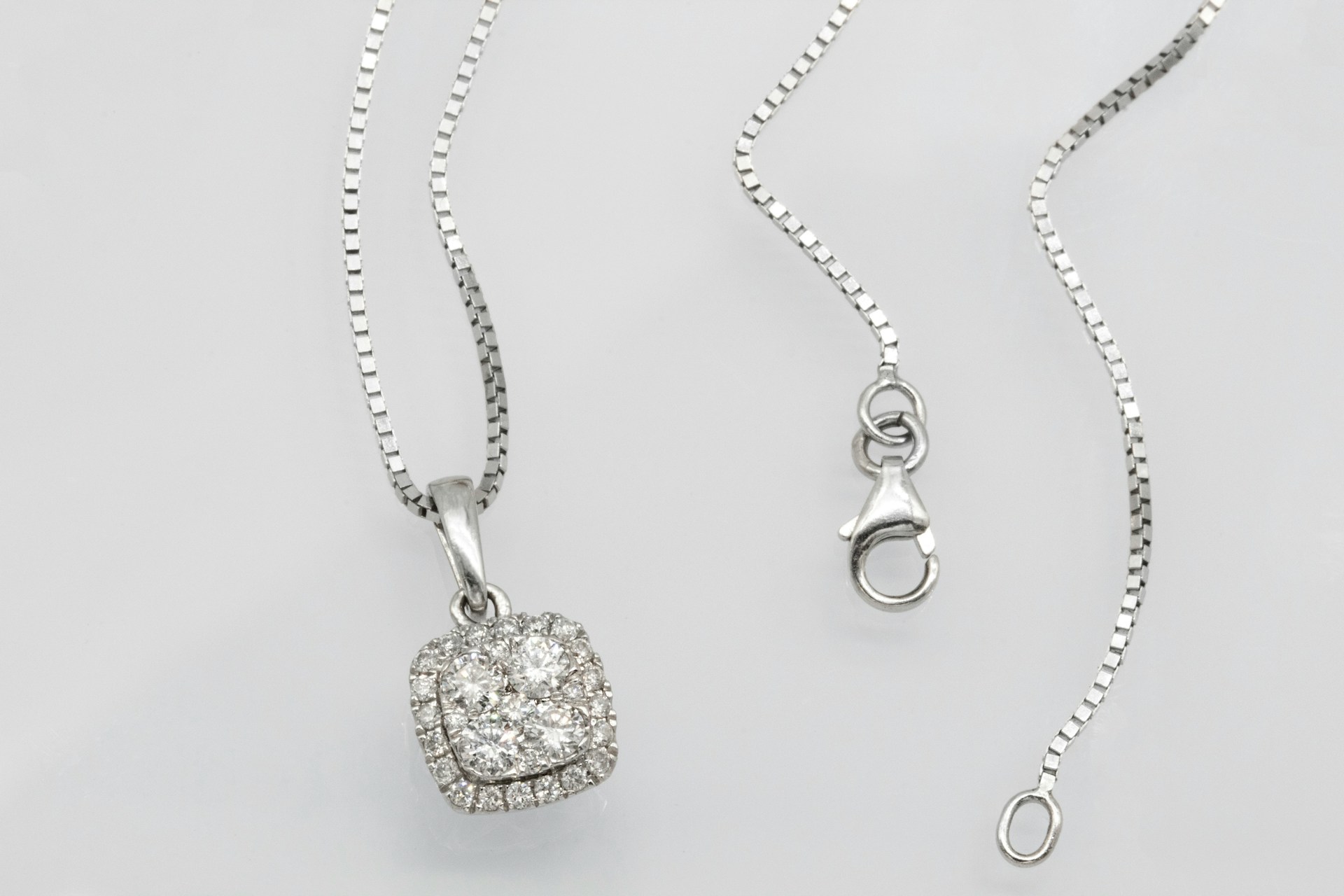 a white gold necklace with a diamond pendant on a gray surface