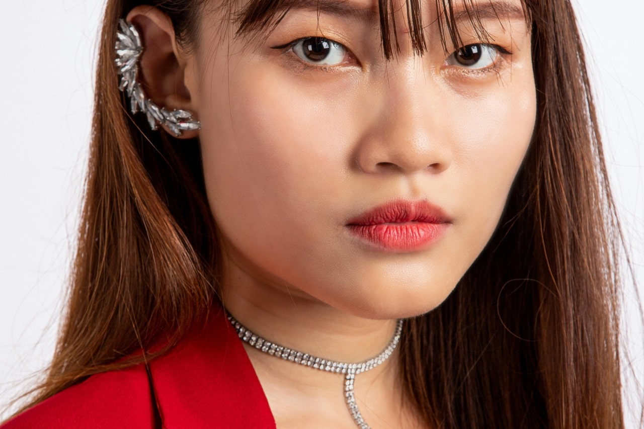 A close-up of a stylish young woman wearing a striking diamond necklace and ear cuff.