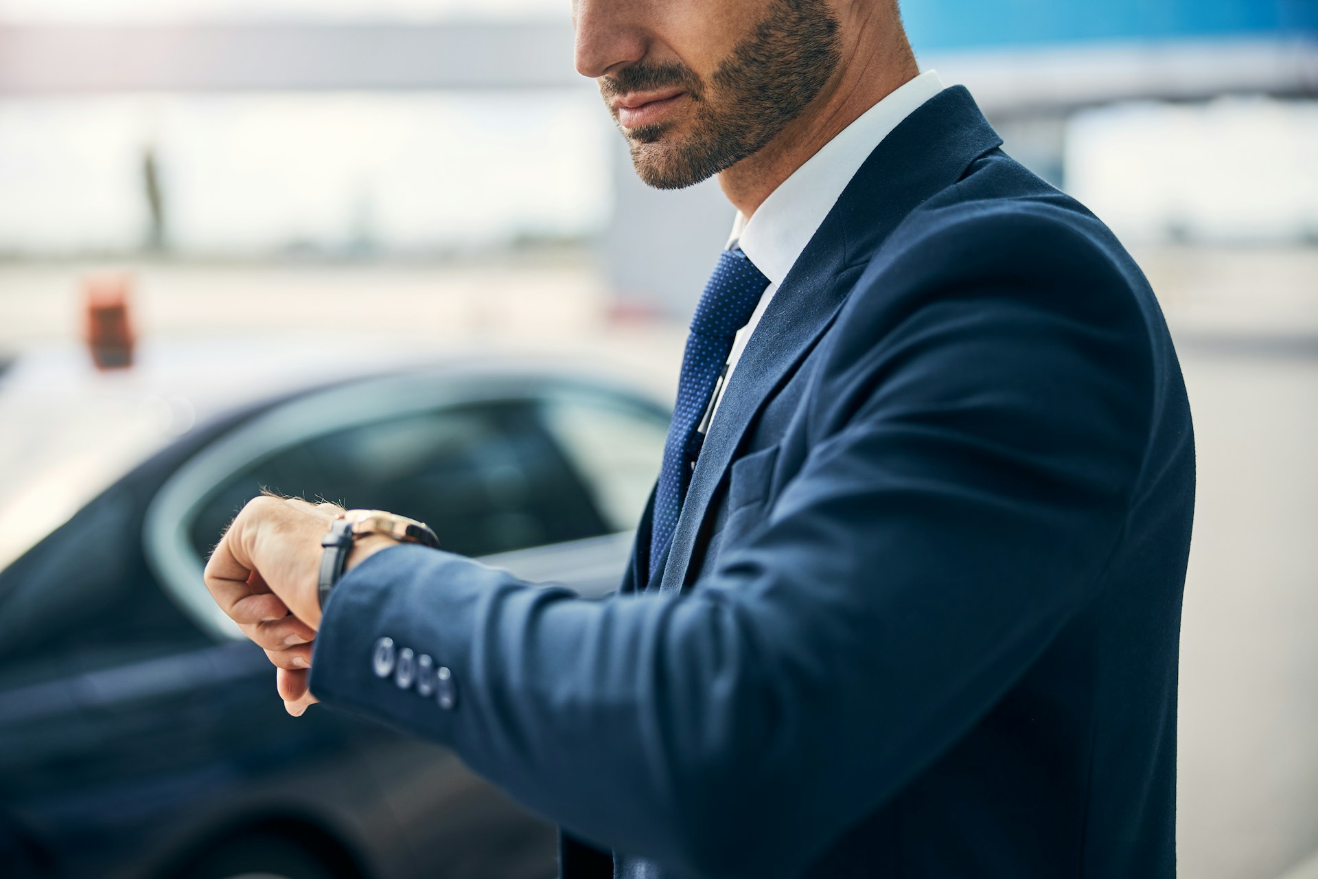 A close-up of a man in a suit checking his watch as he walks to his car.