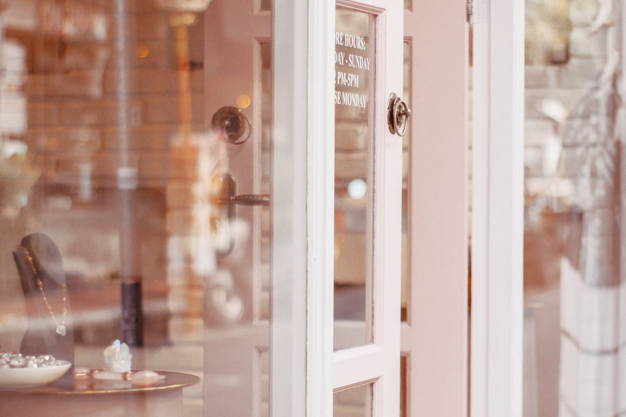 the door and window of a jewelry store with the hours listed in white letters