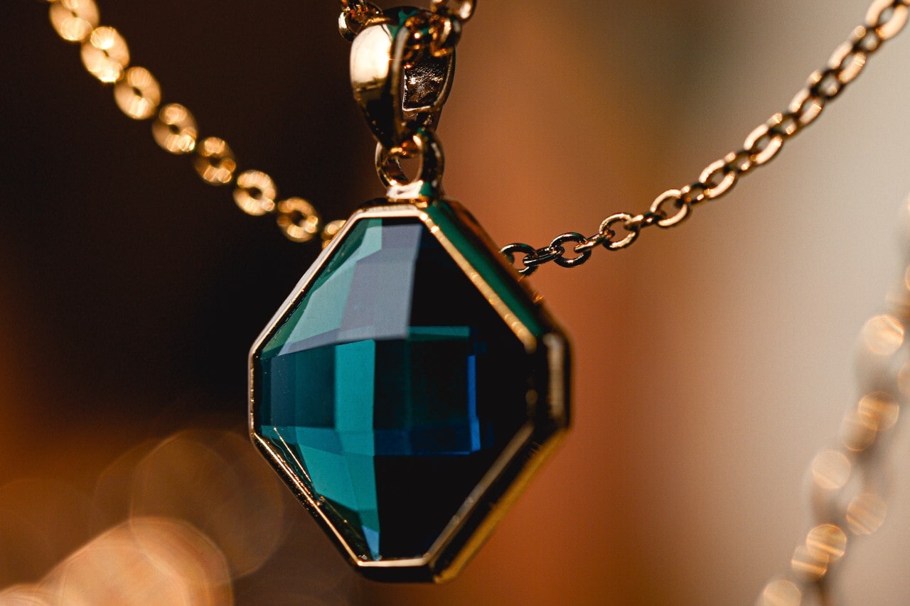 a close up image of a geometric gemstone necklace in a yellow gold setting with a yellow gold chain