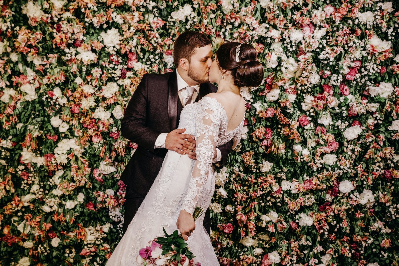 A bride and groom sharing a kiss in front of a flower wall at their venue.
