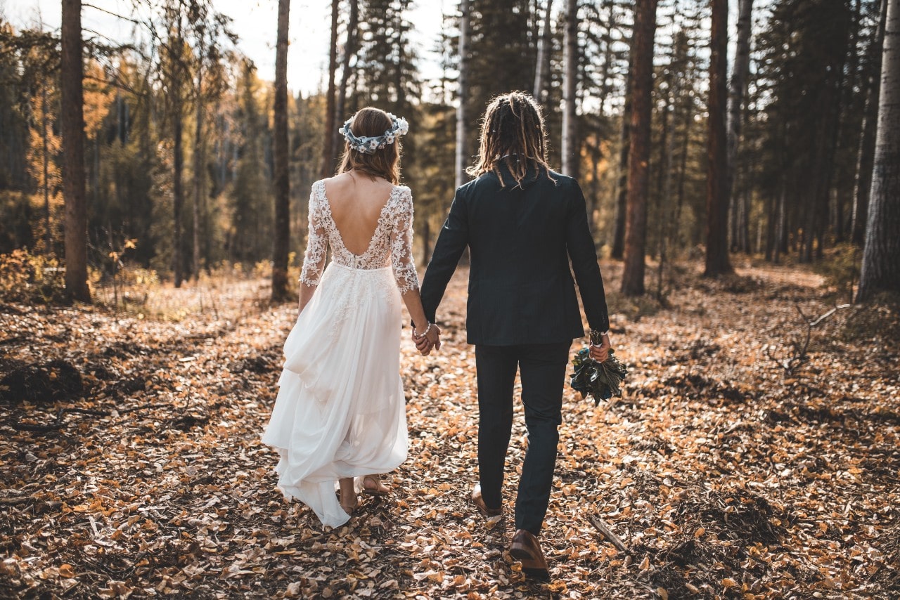 A couple walking through the fall woods on the day of their wedding