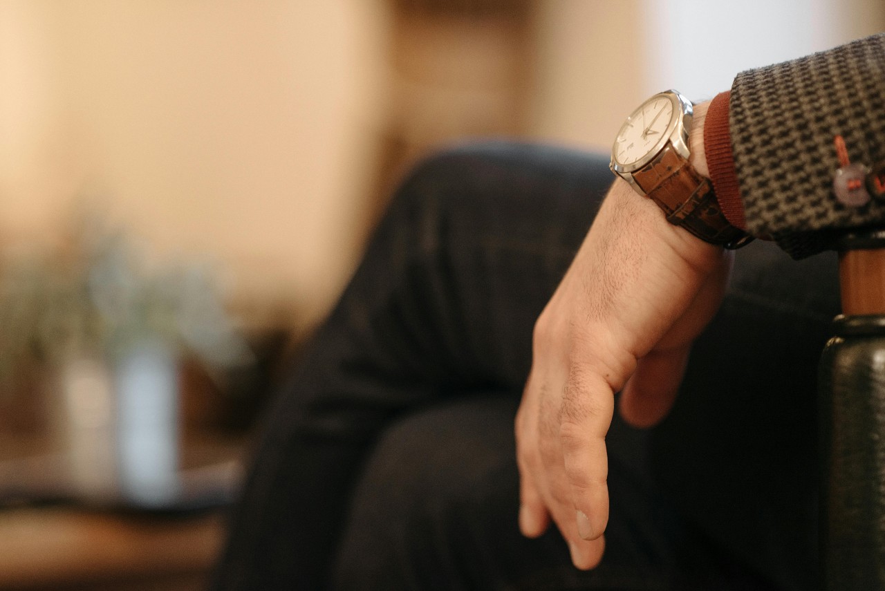 a man sitting in a chair and wearing a silver watch with a brown leather strap