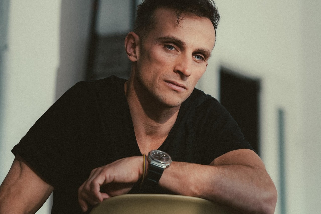 a man sitting backwards in a chair wearing a black t-shirt and a silver watch with a black strap
