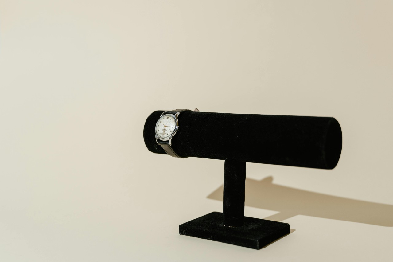 a silver watch with a white dial and black strap on a black velvet stand