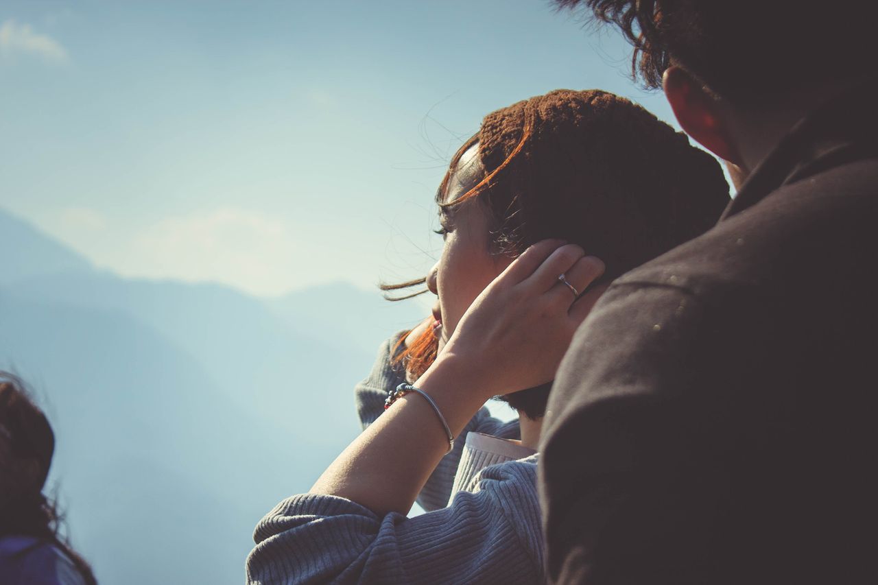 A close-up of a young couple enjoying a breathtaking mountain view, with emphasis on the simple bracelet on the woman’s wrist.