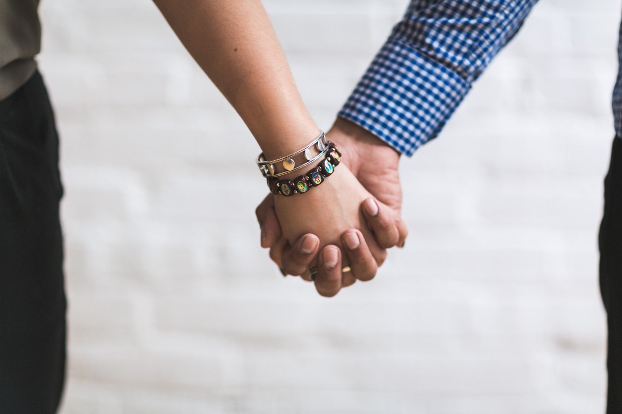 A close-up of a couple holding hands, with distinctive and trendy bracelets on her wrist.