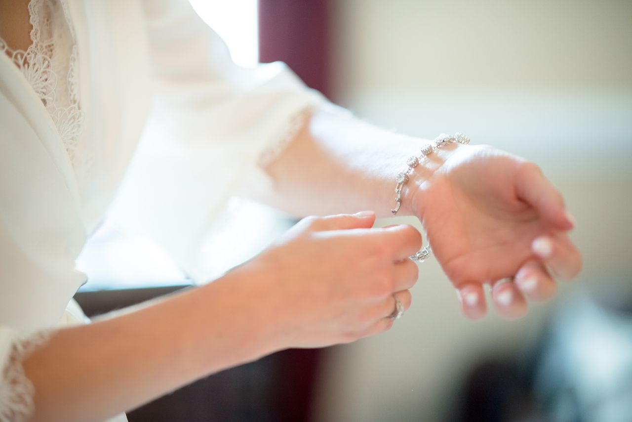 A close-up of a woman wearing a delicate white dress as she puts a diamond bracelet on her wrist.