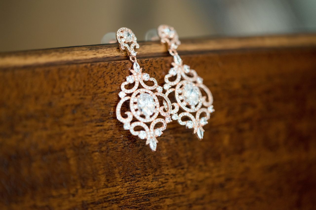 A pair of detailed drop earrings with diamond accents sit on the edge of a wooden table.