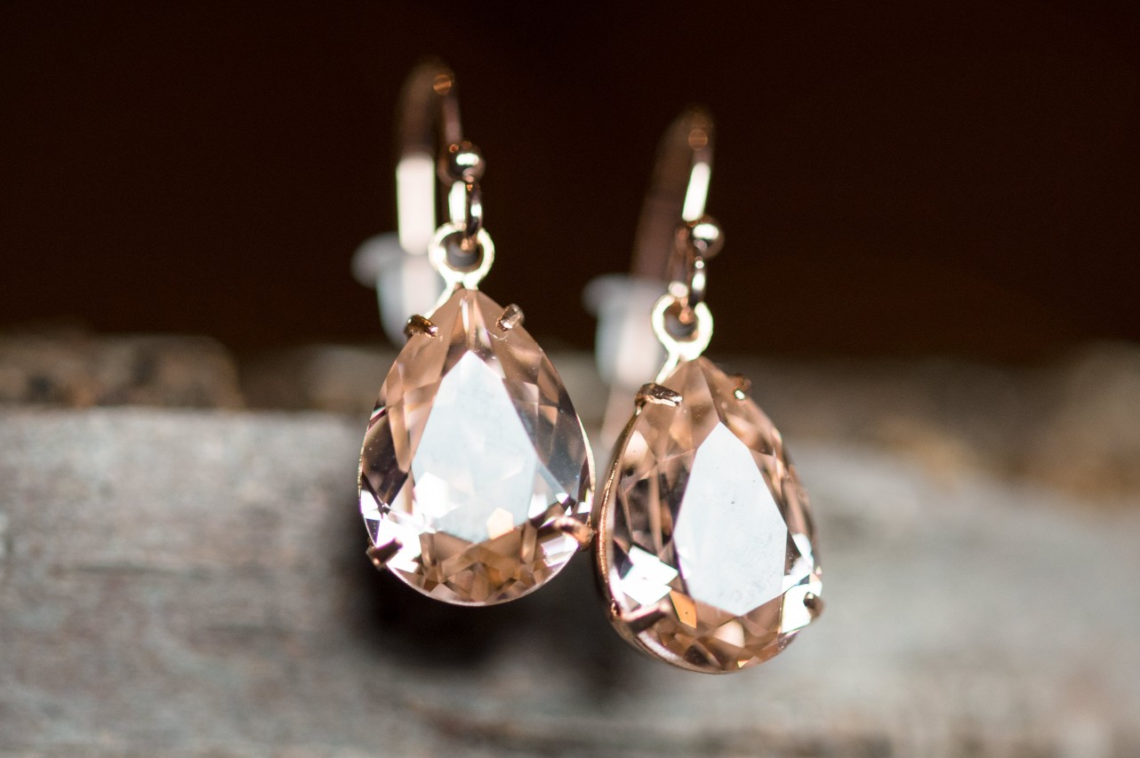A pair of morganite drop earrings hang on the side of a piece of wood.