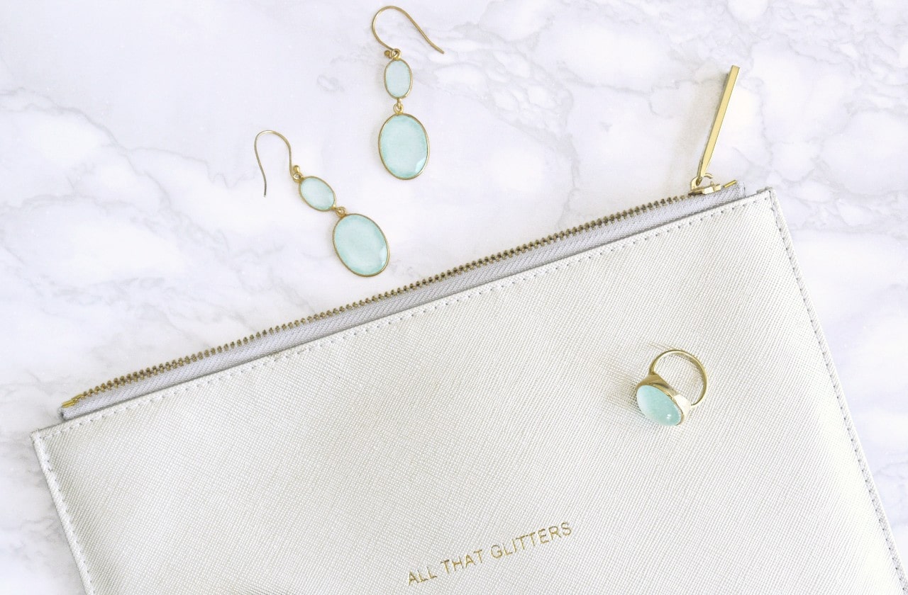 A pair of blue gemstone drop earrings and a matching ring sit on a white bag.