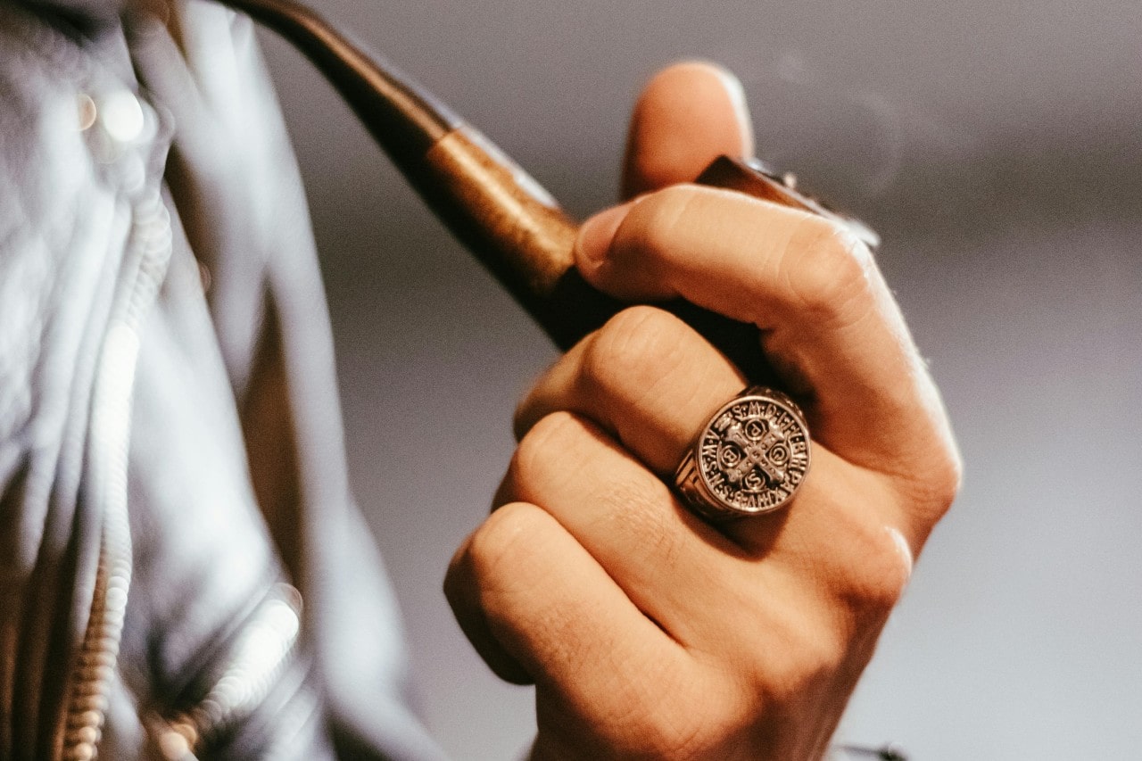a person’s hand holding a pipe and wearing a cross signet ring a person’s hand holding a pipe and wearing a cross signet ring