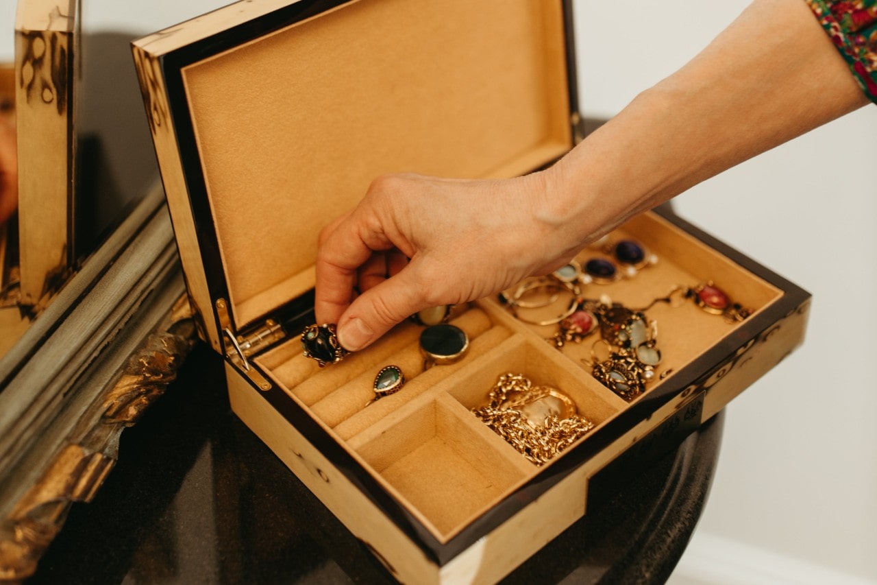 A hand reaching out to a jewelry box that displays an assortment of rings with massive stones, chains, and other fine jewelry. A hand reaching out to a jewelry box that displays an assortment of rings with massive stones, chains, and other fine jewelry.