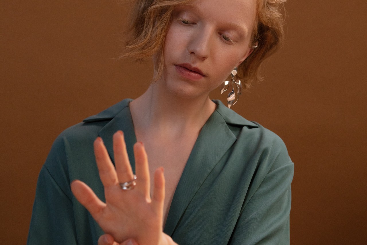A woman with ginger hair with floral earring admiring her rings, sitting against a dark orange wall A woman with ginger hair with floral earring admiring her rings, sitting against a dark orange wall