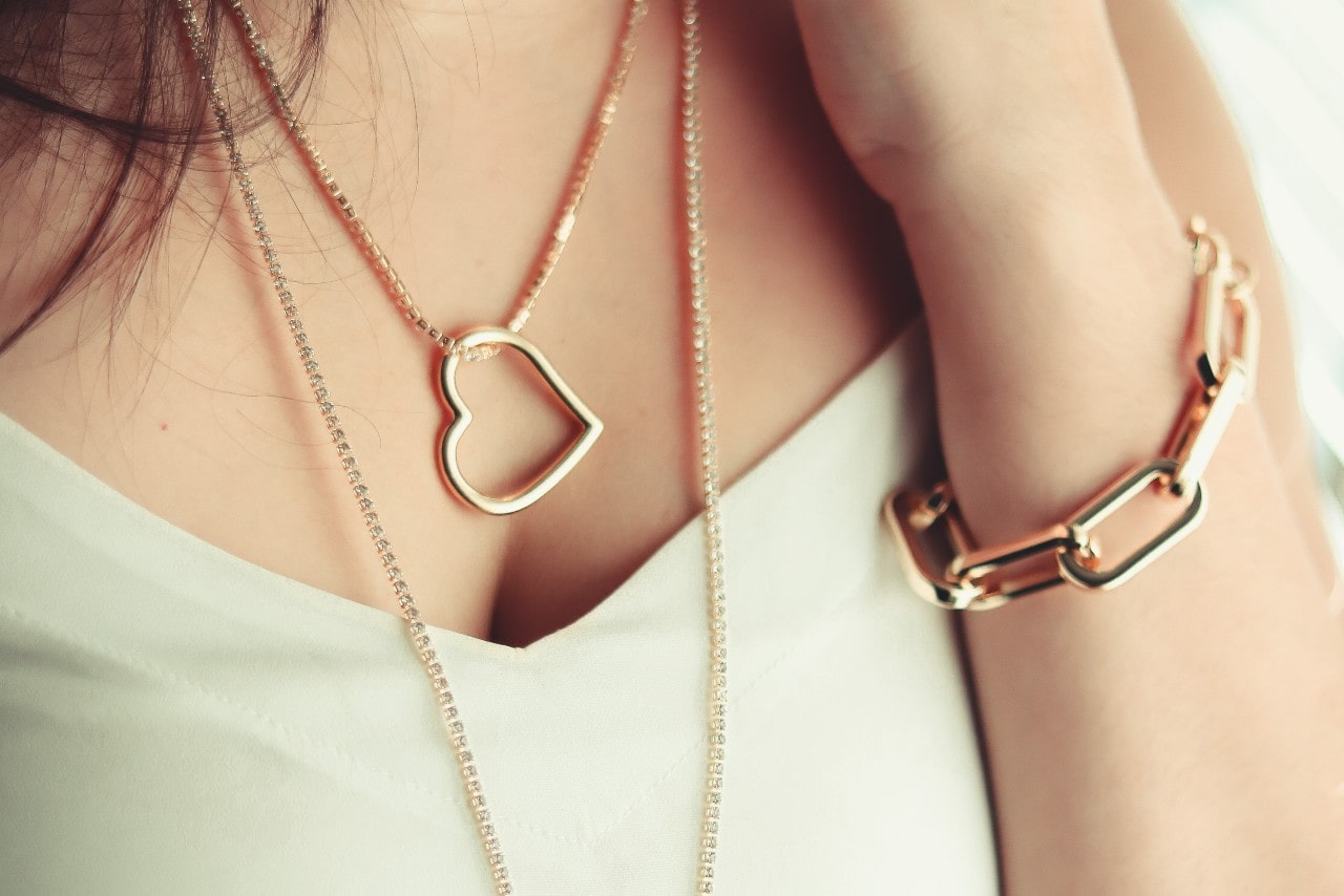 A woman wearing a gold heart-shaped pendant necklace and a chunky gold bracelet on her wrist. A woman wearing a gold heart-shaped pendant necklace and a chunky gold bracelet on her wrist.