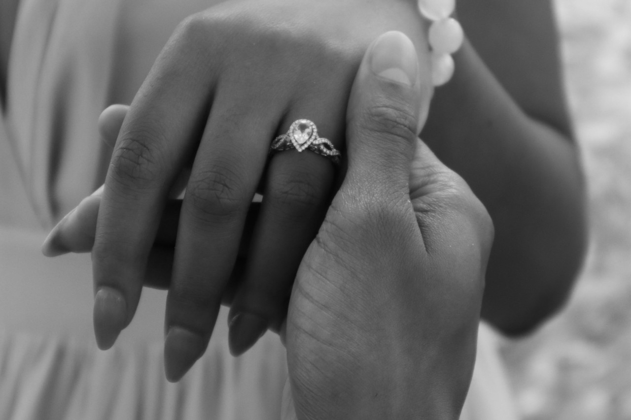 A black-and-white photo showing a woman’s hand showcasing a pear-cut diamond ring, while being held, highlighting the ring’s twisted band design.