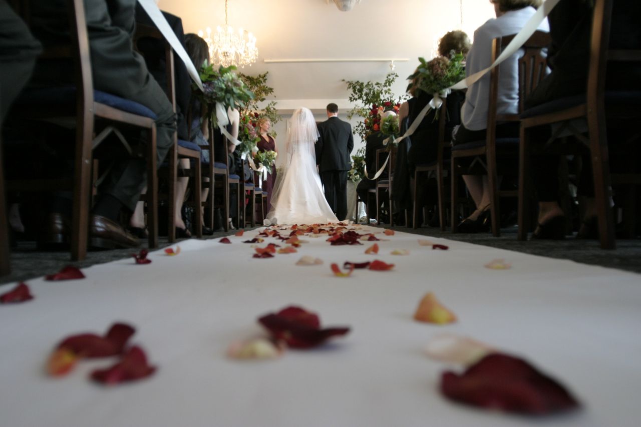 a bride walks down the aisle in a church, rose petals strewn across the aisle.