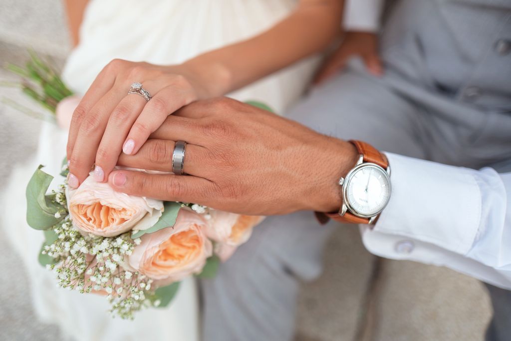 A couple rests their hands on a bouquet, showing their wedding rings.