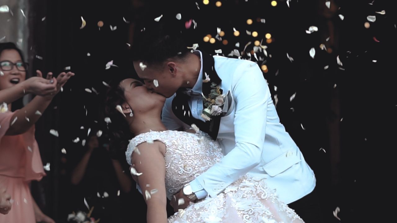 A bride and groom kiss as guests throw confetti their way.