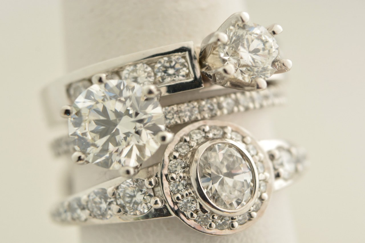 A stack of three sparkling diamond rings with intricate designs and bright round stones, set against a cream colored background. A stack of three sparkling diamond rings with intricate designs and bright round stones, set against a cream colored background.