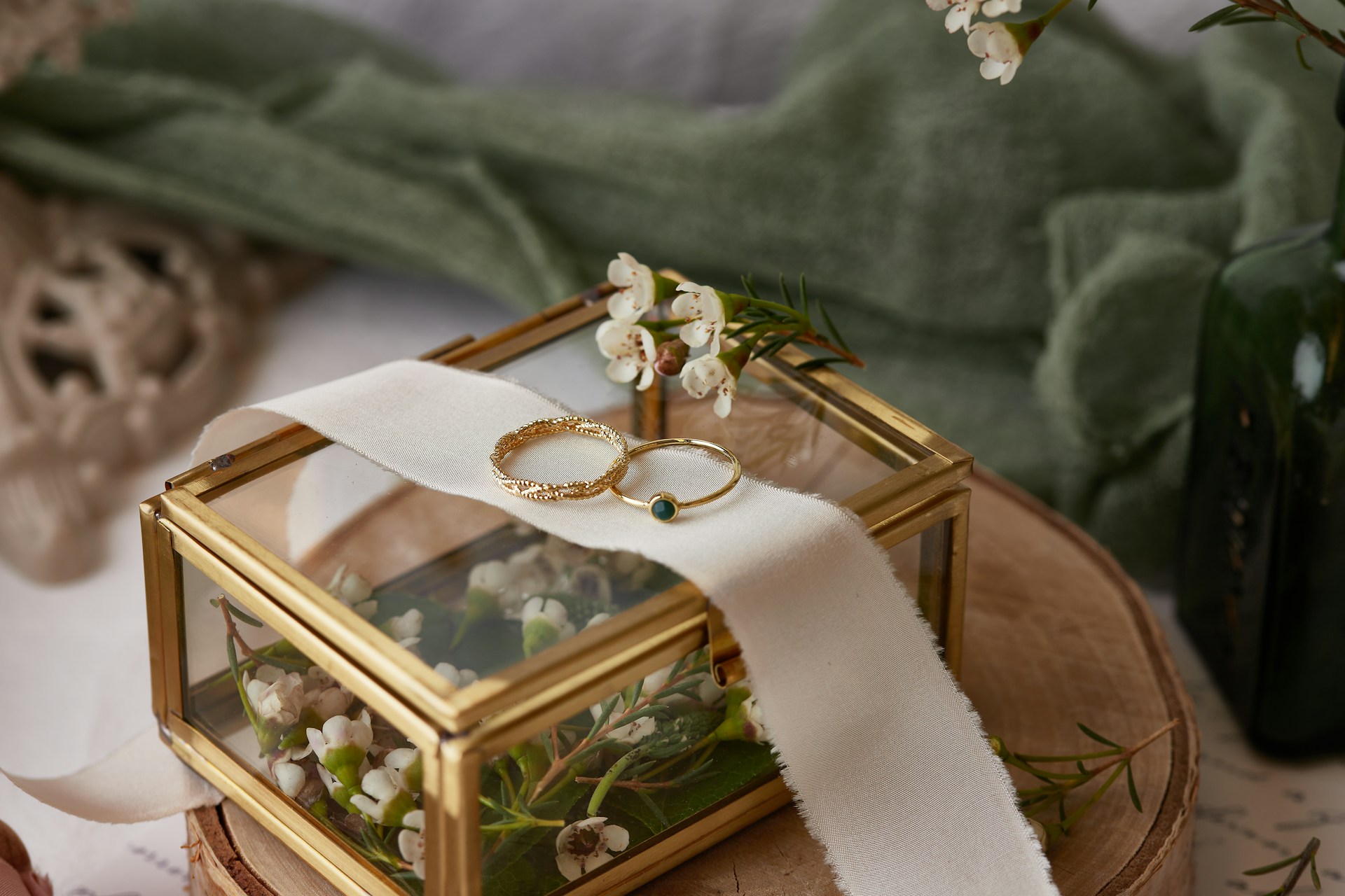 Two elegant gold bands resting on a white ribbon atop a glass box filled with flowers. Two elegant gold bands resting on a white ribbon atop a glass box filled with flowers.