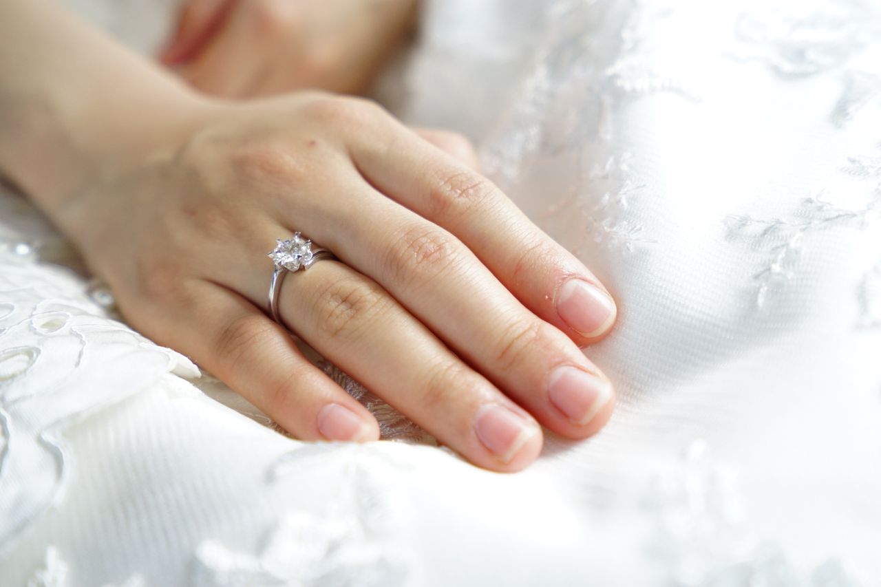 A close-up of a bride’s hand atop her wedding dress, adorned with a solitaire engagement ring. A close-up of a bride’s hand atop her wedding dress, adorned with a solitaire engagement ring.